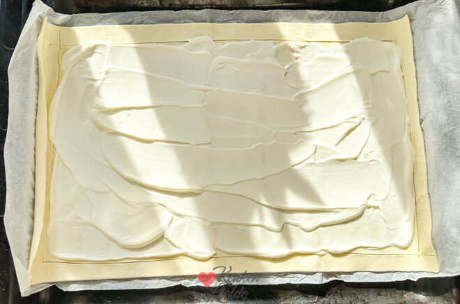 Bladerdeeg insnijden en bestrijken met crème fraîche en parmezaan